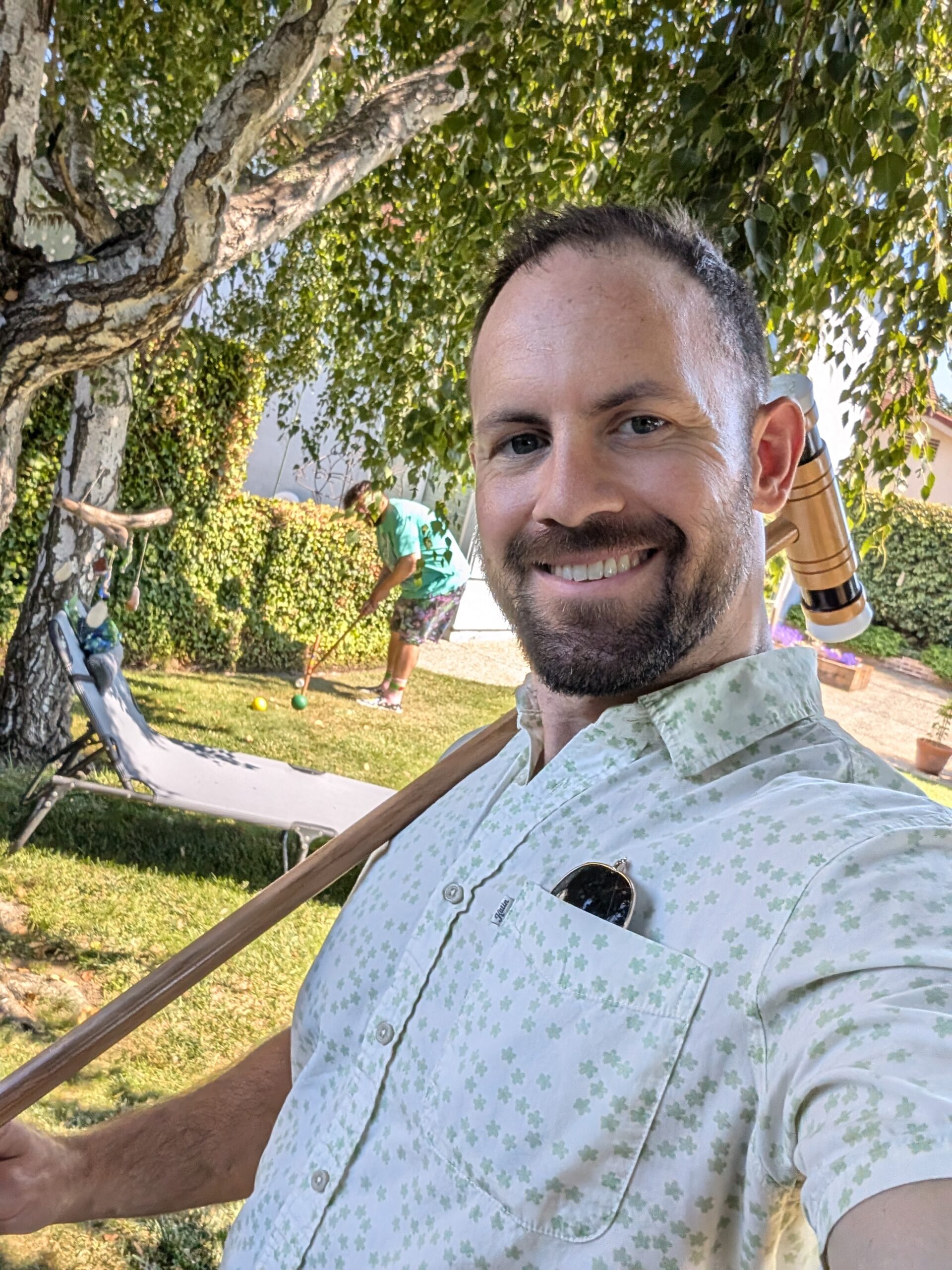 Nick Kostalas smiles, standing in a backyard holding a croquet mallet